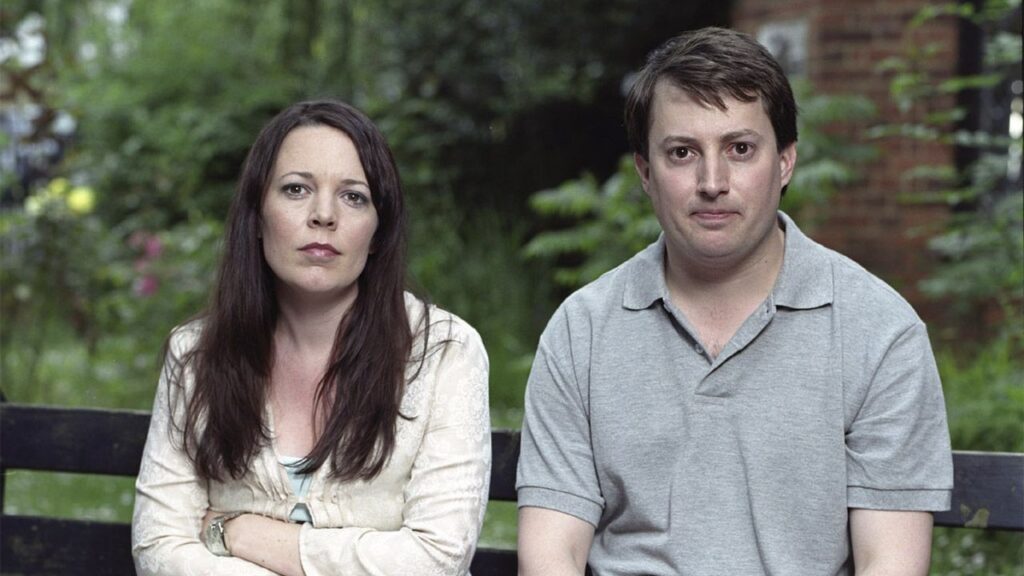 Olivia Colman y David Mitchell, quienes hicieron de Sophie y Mark en la serie Peep Show. Sentados en una banca, viendo a la cámara con seriedad y algo de preocupación.
