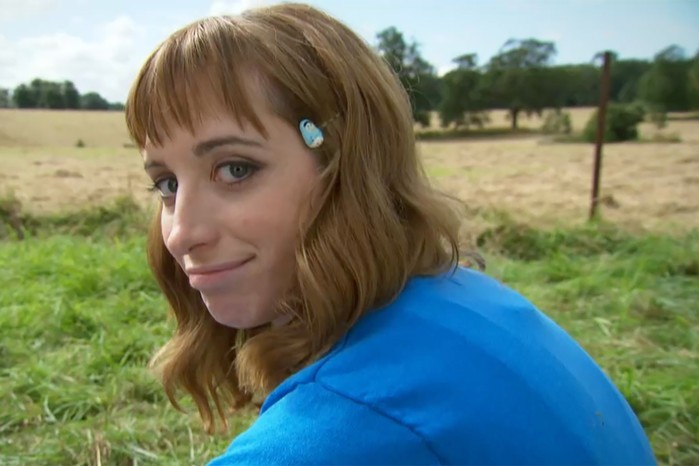 Isy Suttie como Dobbie sentada en el pasto y mirando al espectador con penita en la serie Peep Show.