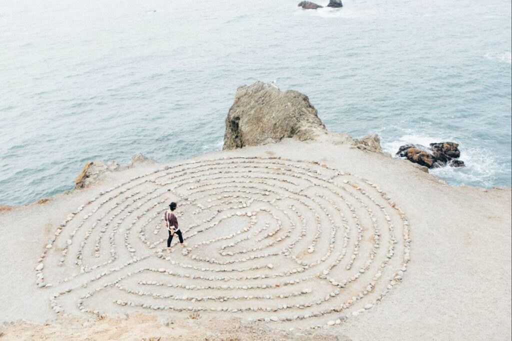 Una persona en la playa, en medio de un laberinto hecho con piedras pequeñas.