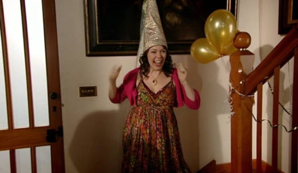 Olivia Colman como Sophie celebrando su cumpleaños con un gorrito en forma de cono en casa de su familia en la serie Peep Show.